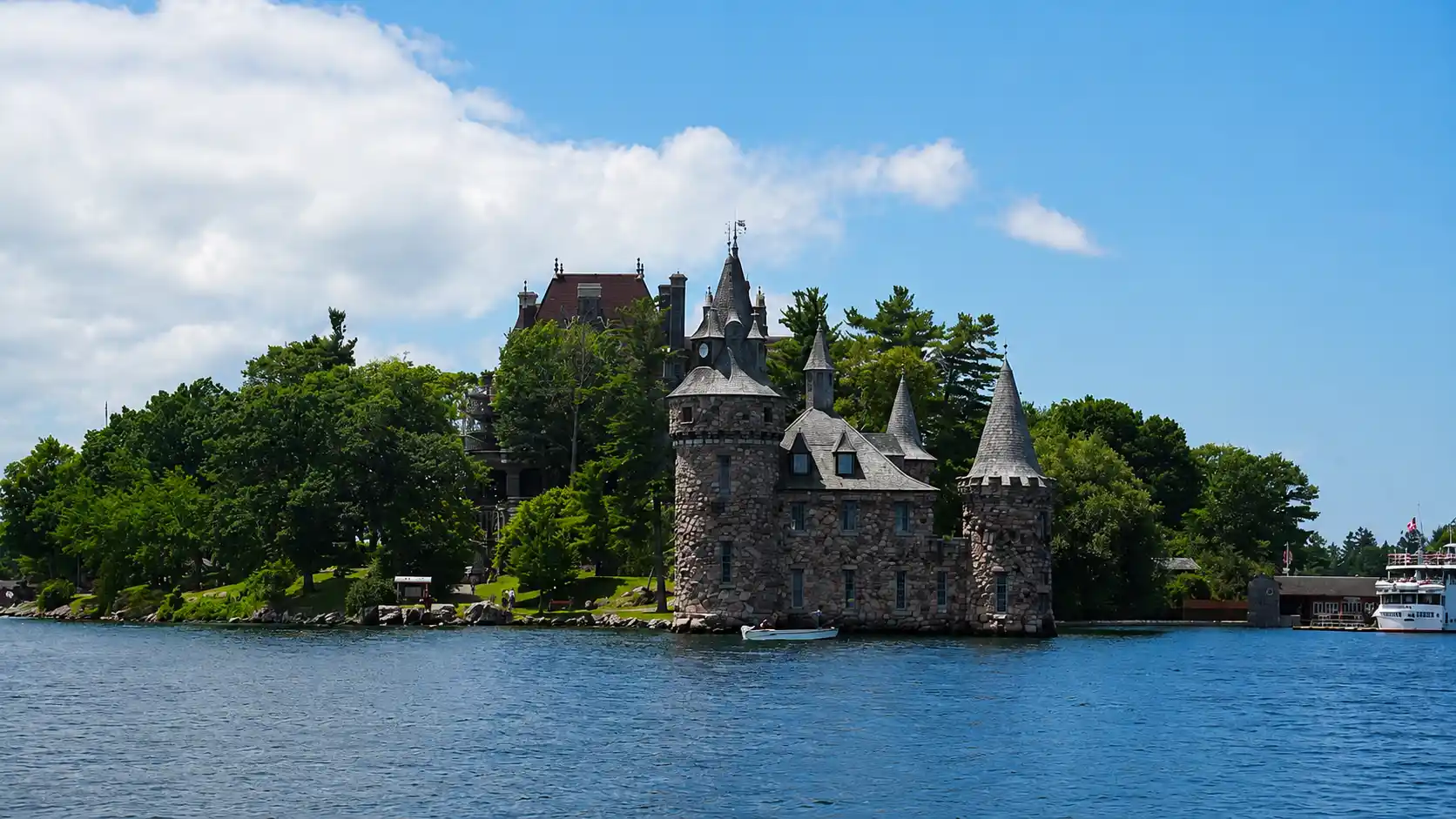 Passengers on the open upper deck of a sightseeing boat cruising past forested islands on the St. Lawrence River
