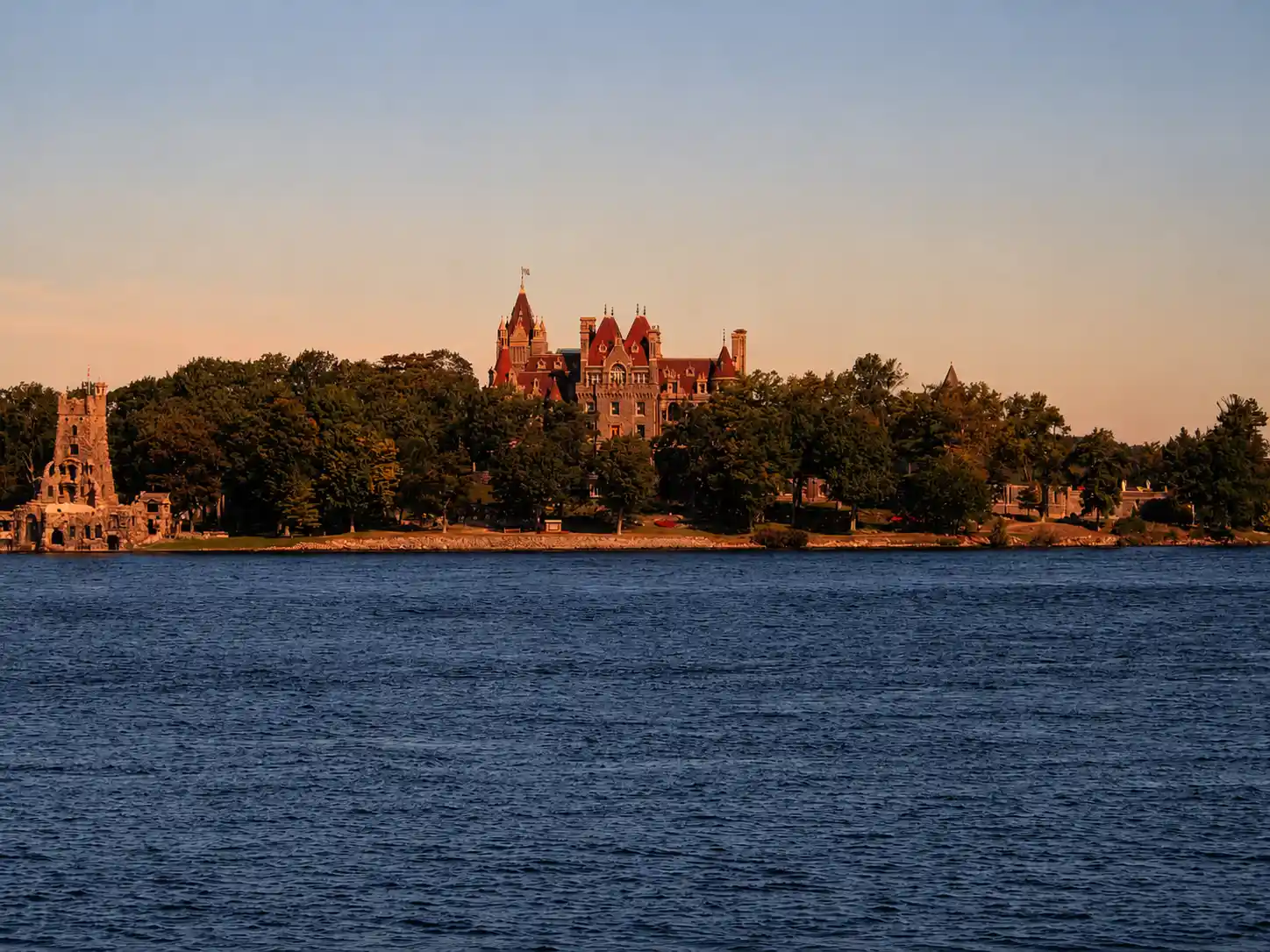 Illuminated passenger tour boat cruising past forested islands on the St. Lawrence River at twilight