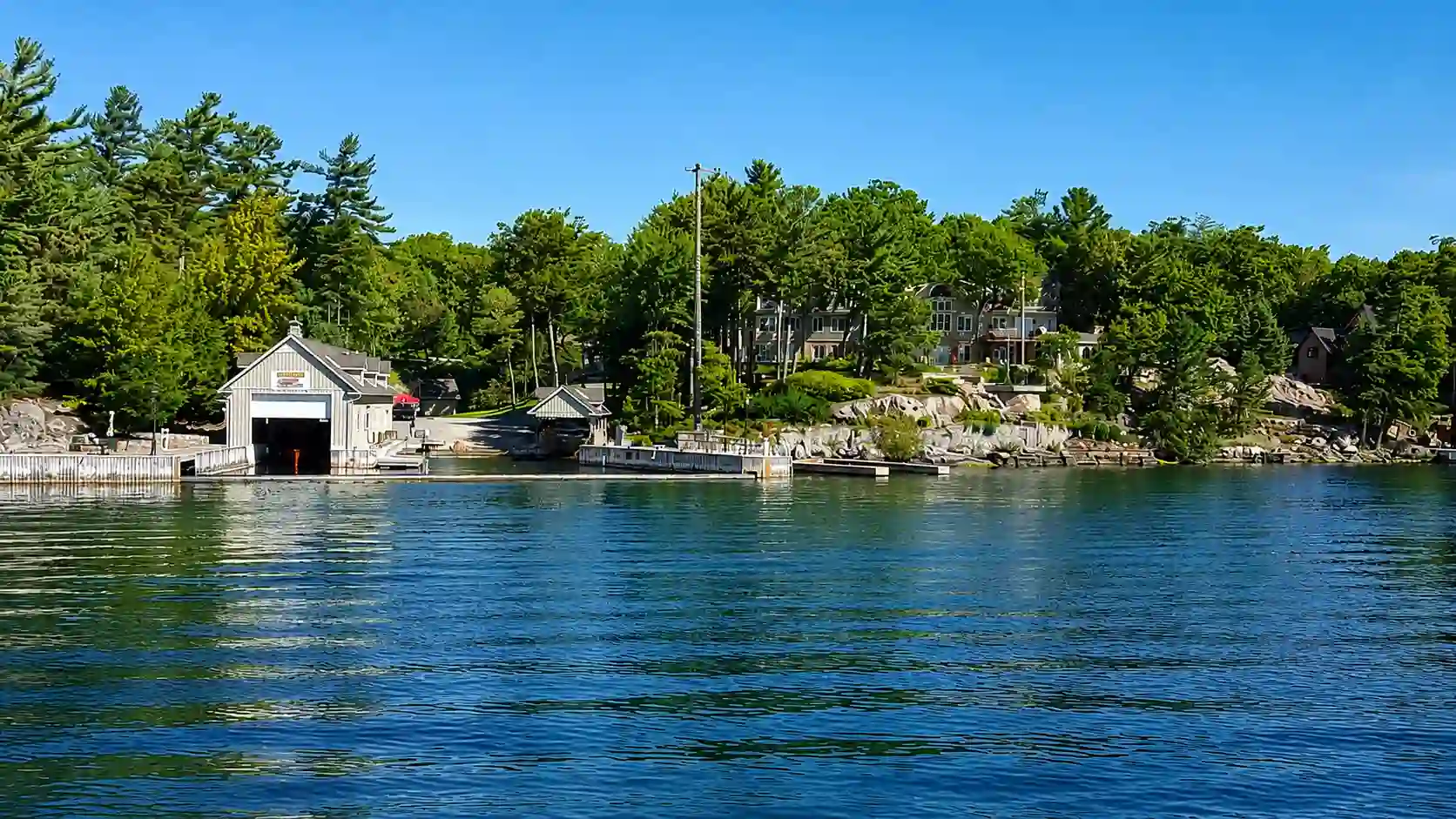 Gilded Age waterfront mansions and boathouses lining a river shoreline in golden evening light