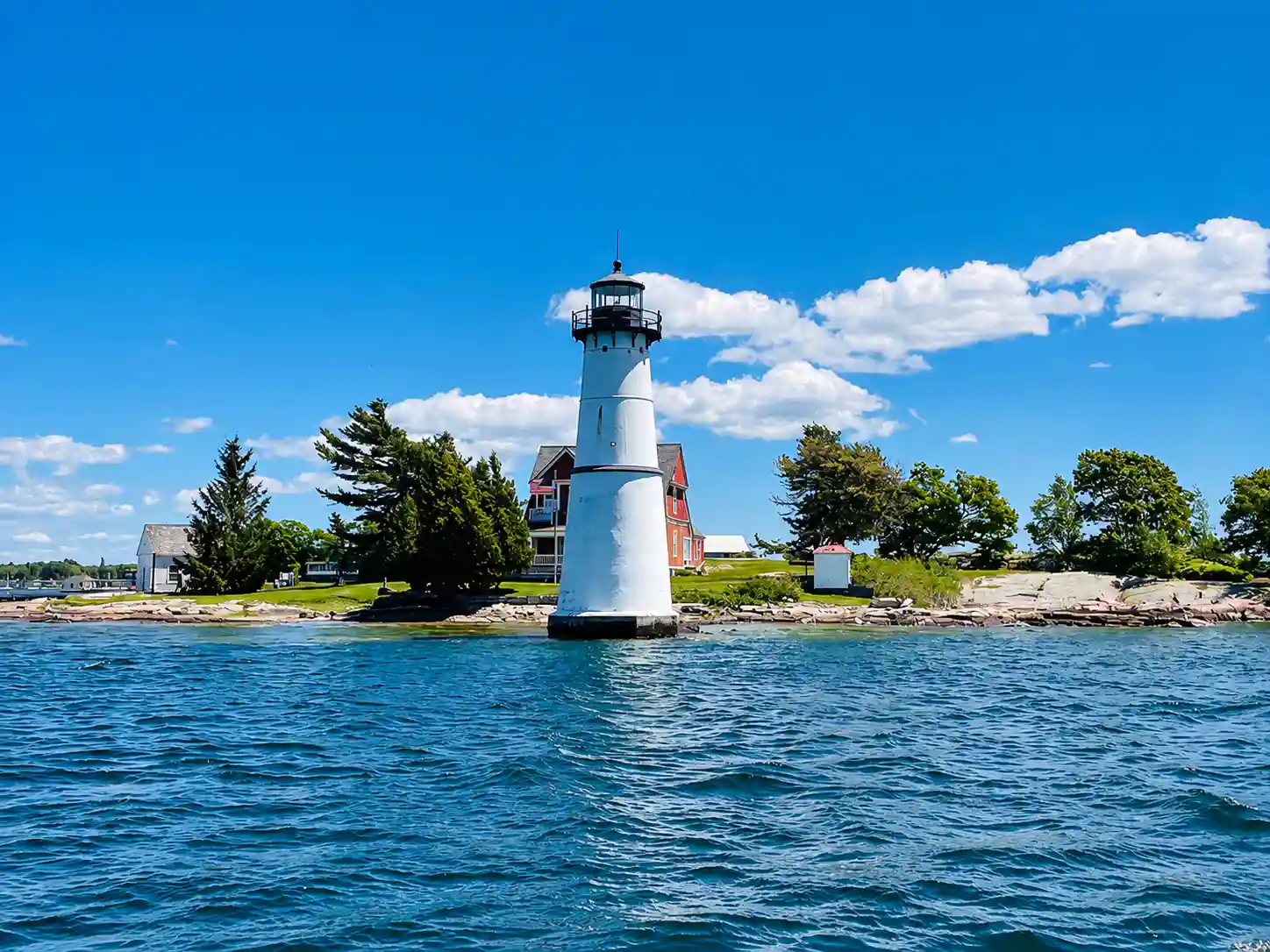 White stone lighthouse on a tiny island surrounded by clear shallow turquoise water